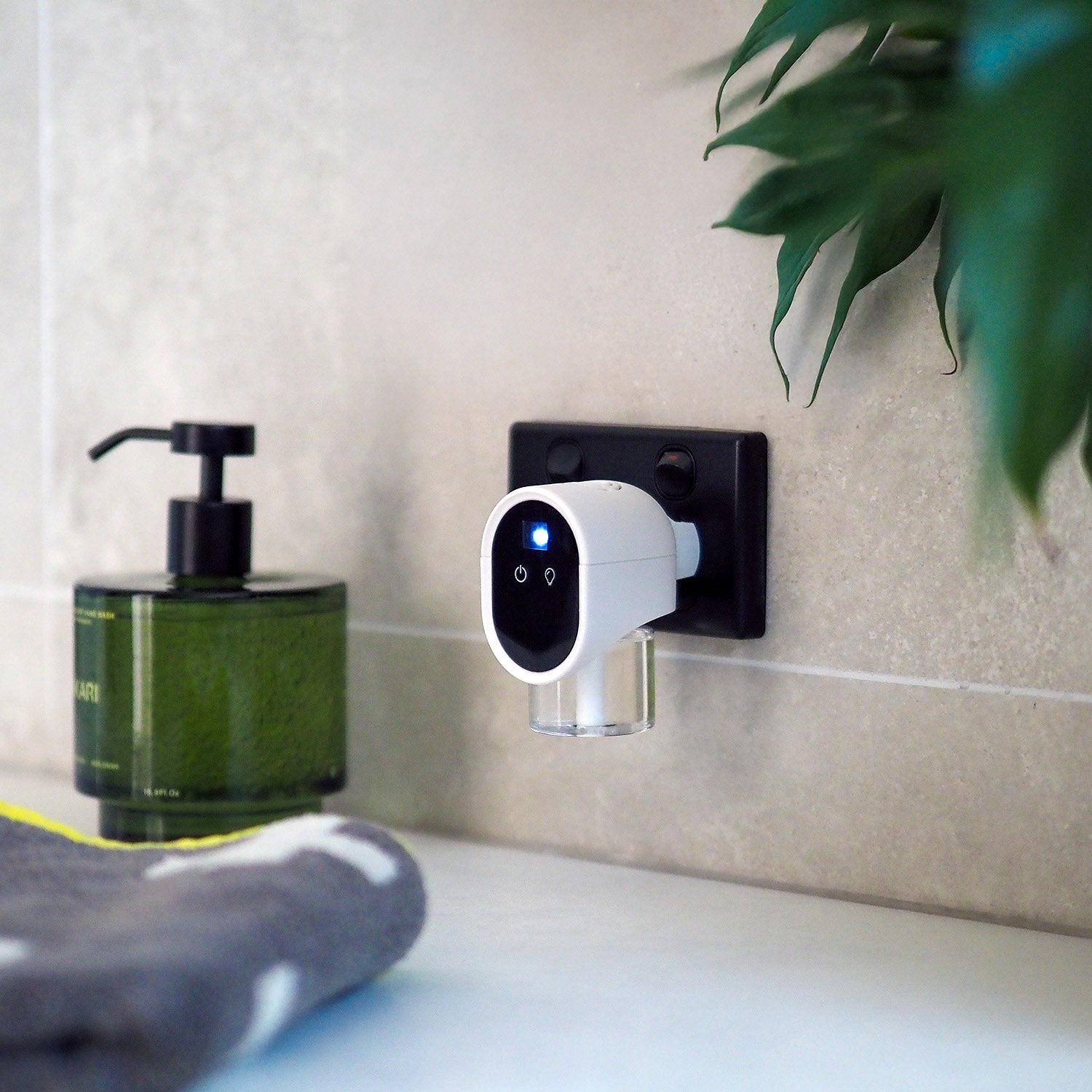 Smart plug-in air freshener on a wall next to a bottle of soap and a towel